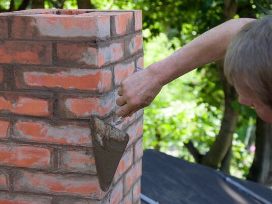 Masonry contractor using a trowel to smooth down the sides of a brick chimney in Oakville, Ontario